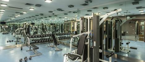 A gym with mirrored walls, various exercise equipment, and dumbbells.