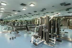 A gym with mirrored walls, various exercise equipment, and dumbbells.