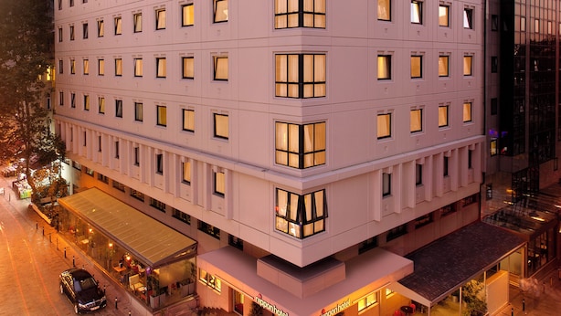 Un hotel de varios pisos con una fachada moderna, amplias ventanas y una entrada a nivel de suelo con una escalera.