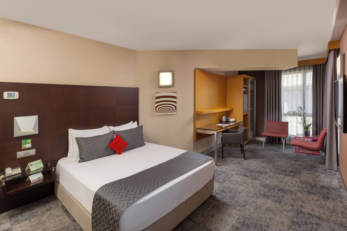 A hotel room with a large bed, a desk, a chair, a small table, and a window with curtains.
