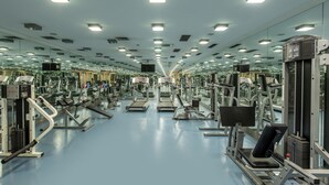 Un gimnasio con diversas máquinas de ejercicio, espejos en las paredes y suelo azul.