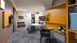 Una habitación de hotel moderna con una cama, un escritorio, una silla, un televisor y un pequeño rincón de descanso.