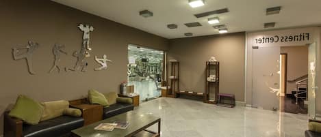 A modern lobby with a reception desk, seating area, and a glass wall offering a view of the gym.