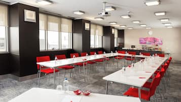 A conference room with white tables, red chairs, and a projector on the ceiling.