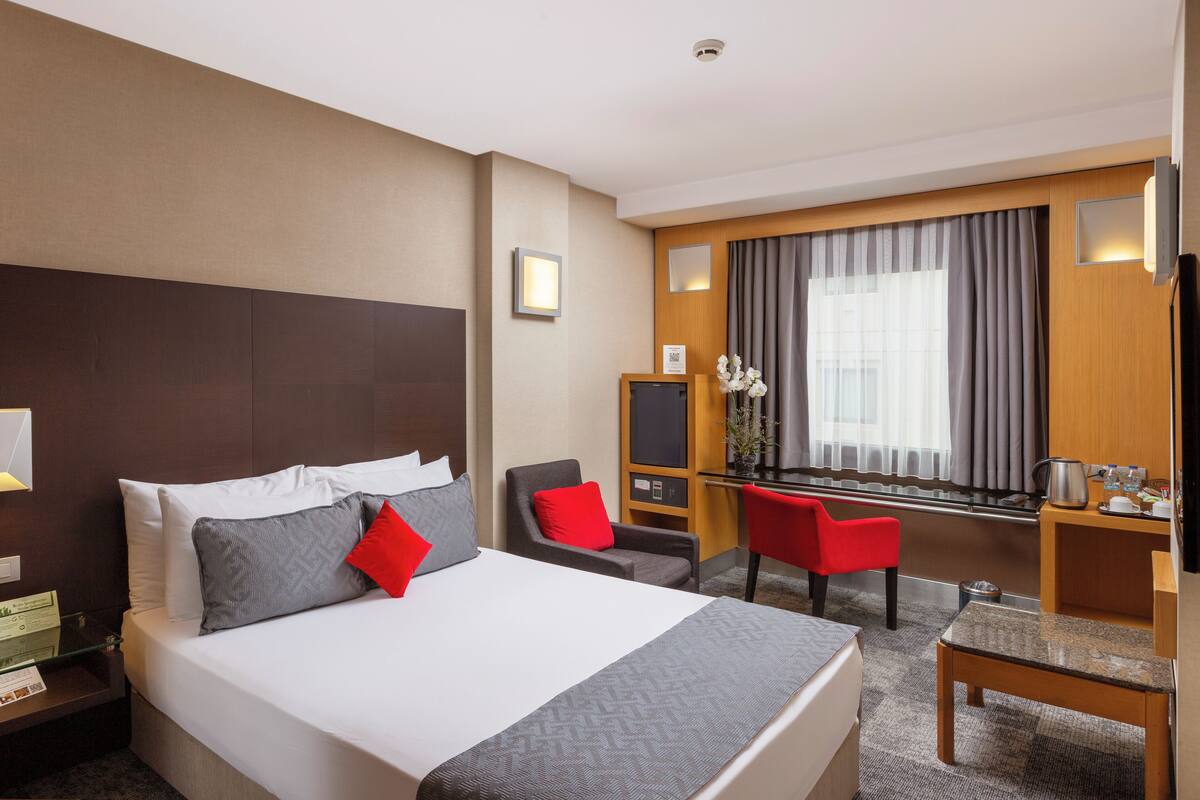 A hotel room with a large bed, a desk, a chair, and a TV.