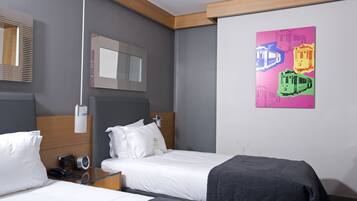 A hotel room with two beds, a bedside table with a phone, a mirror, and a colorful artwork on the wall.