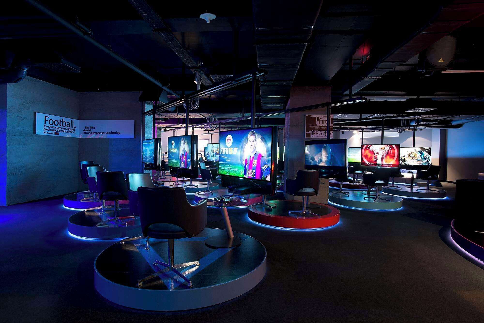 A gaming lounge with multiple screens displaying various video games, including FIFA and Grand Theft Auto.