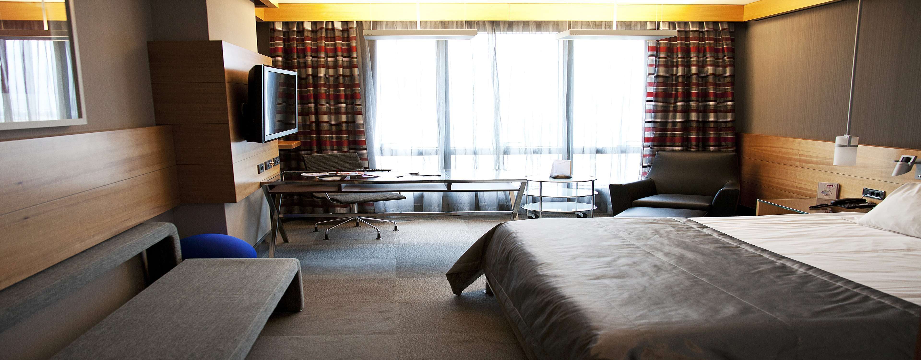 Une chambre d’hôtel avec un lit, un bureau et une chaise, une télévision et une fenêtre avec des rideaux.