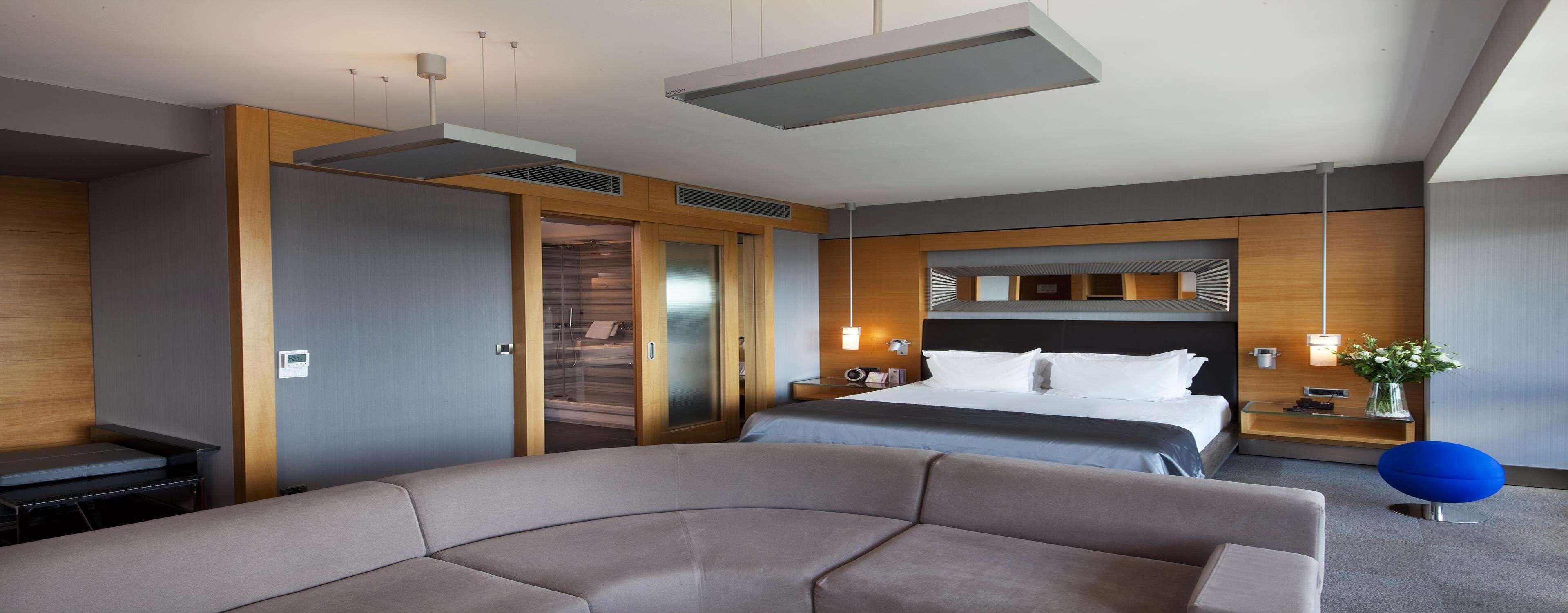 A modern hotel room with a large bed, a sofa, a desk, and a wardrobe.