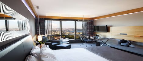 Habitación de hotel moderna con una cama grande, un escritorio con silla, televisión y vistas a la ciudad.
