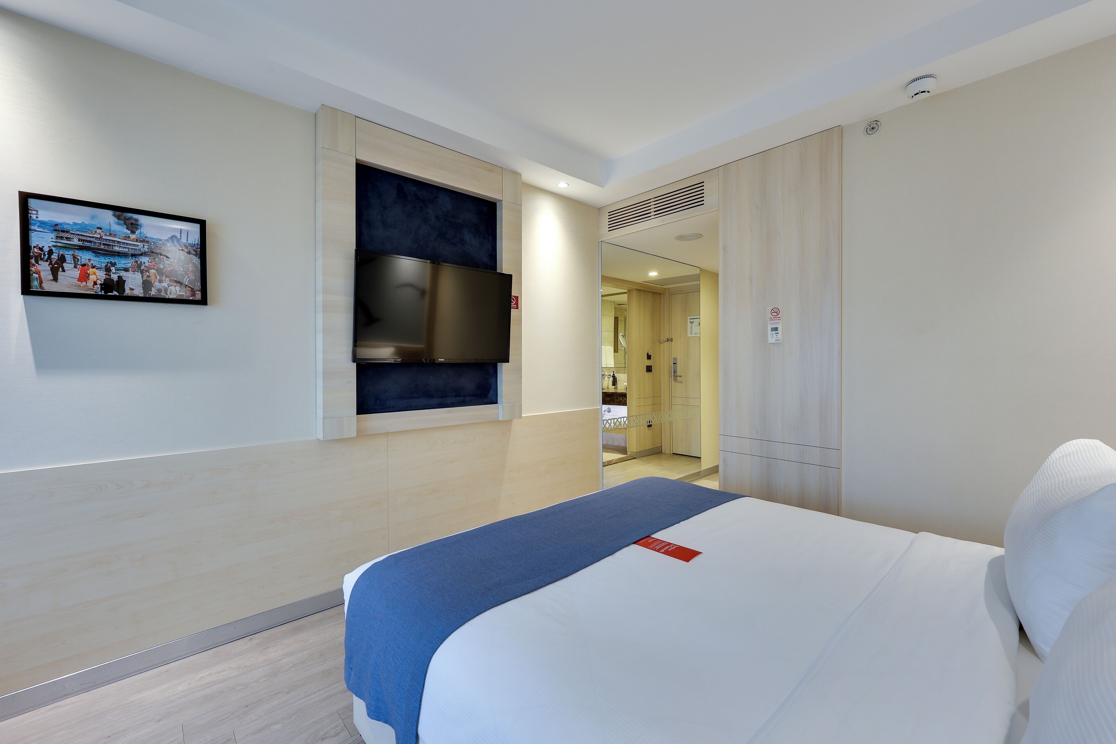 A hotel room with a bed, a TV mounted on the wall, and a picture of a cruise ship.