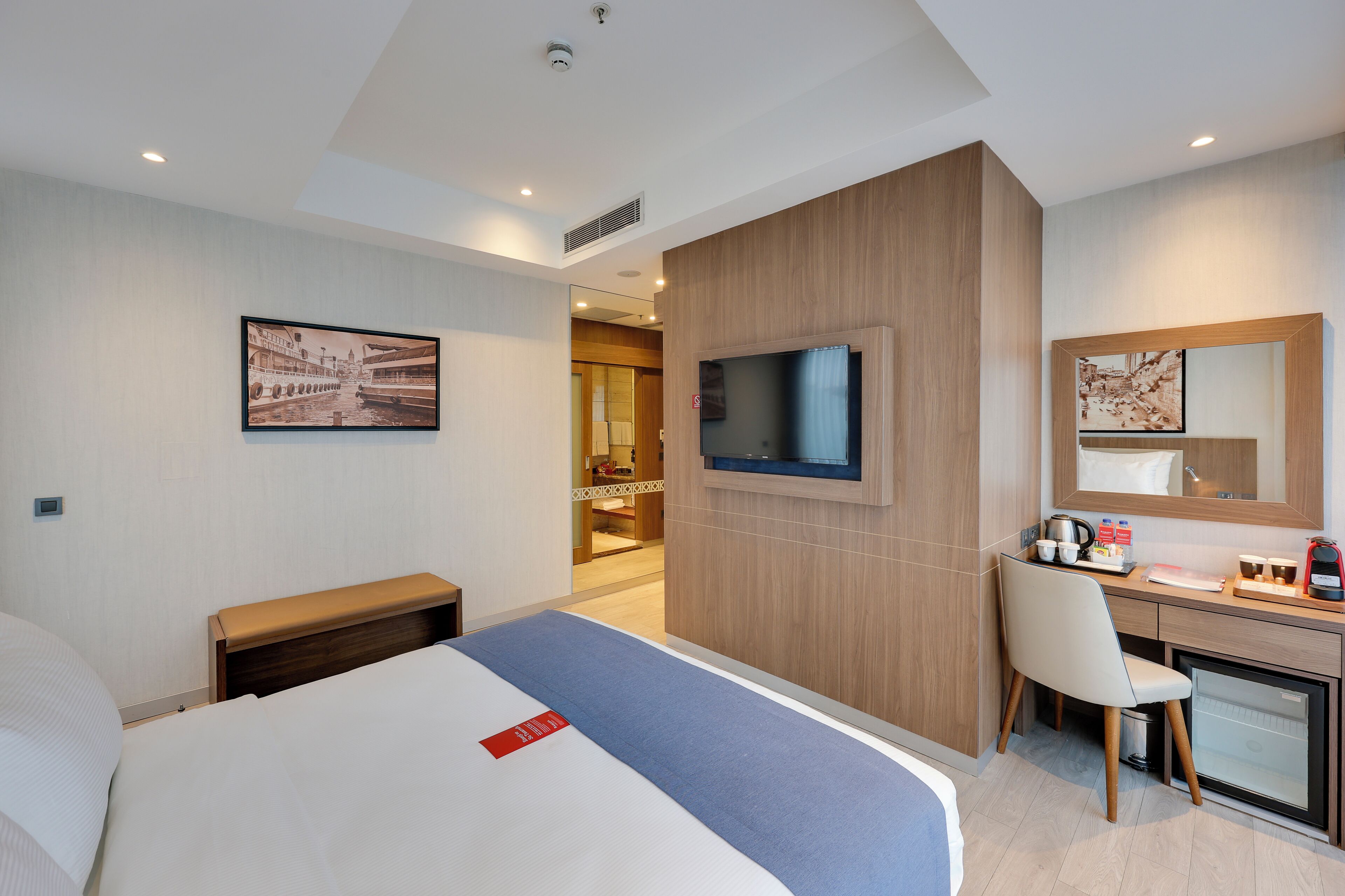 A hotel room with a bed, a desk, a chair, a television, and a small refrigerator.