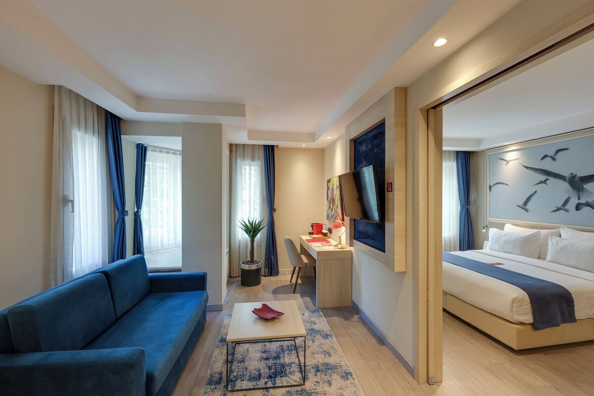 A modern hotel room with a sofa, a desk, a bed, and a TV.