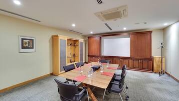 Un salón de conferencias con una larga mesa, sillas, una pantalla de proyector y un perchero.
