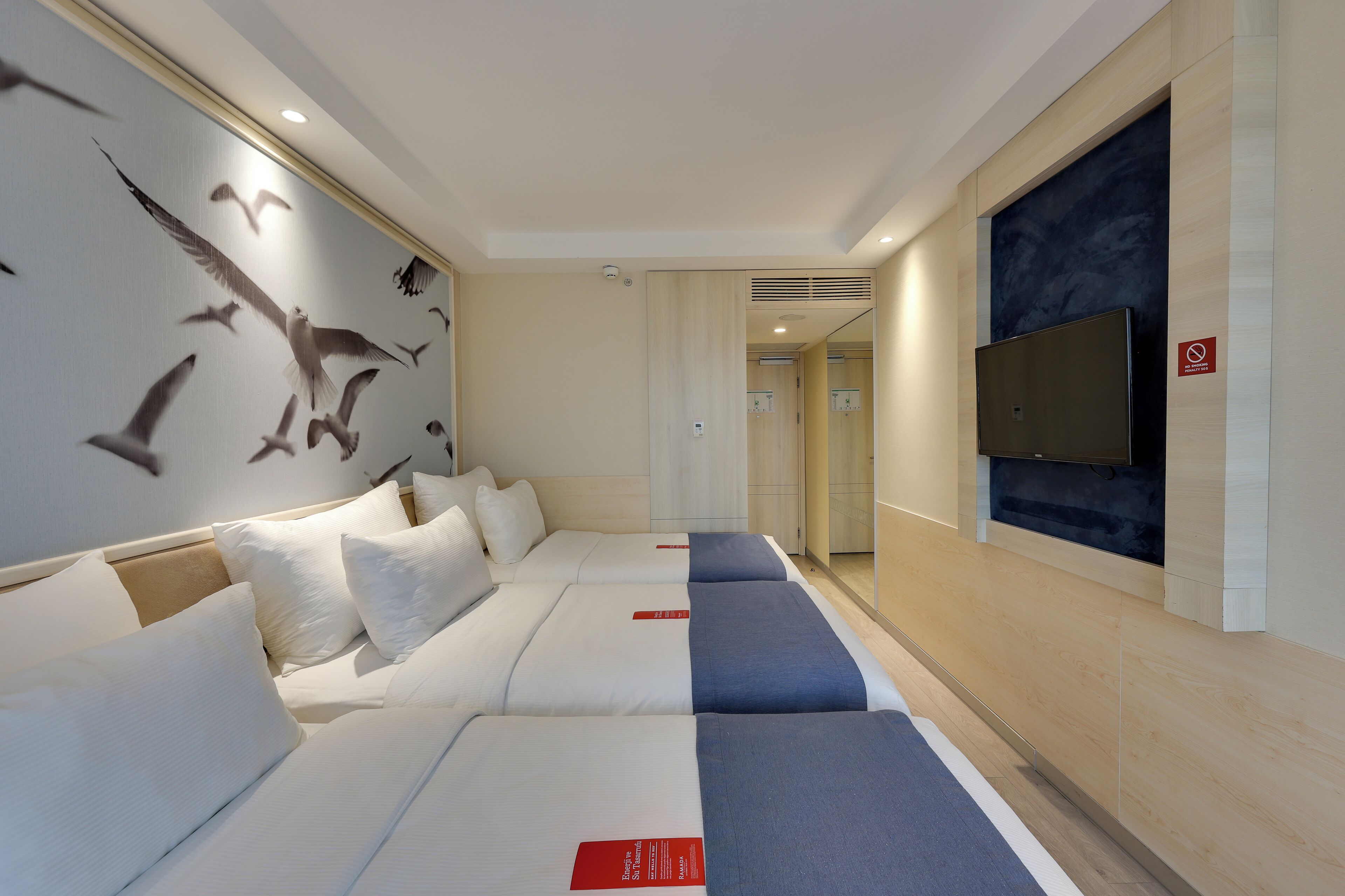 A hotel room with a large bed, a TV mounted on the wall, and a mural of birds on the wall.