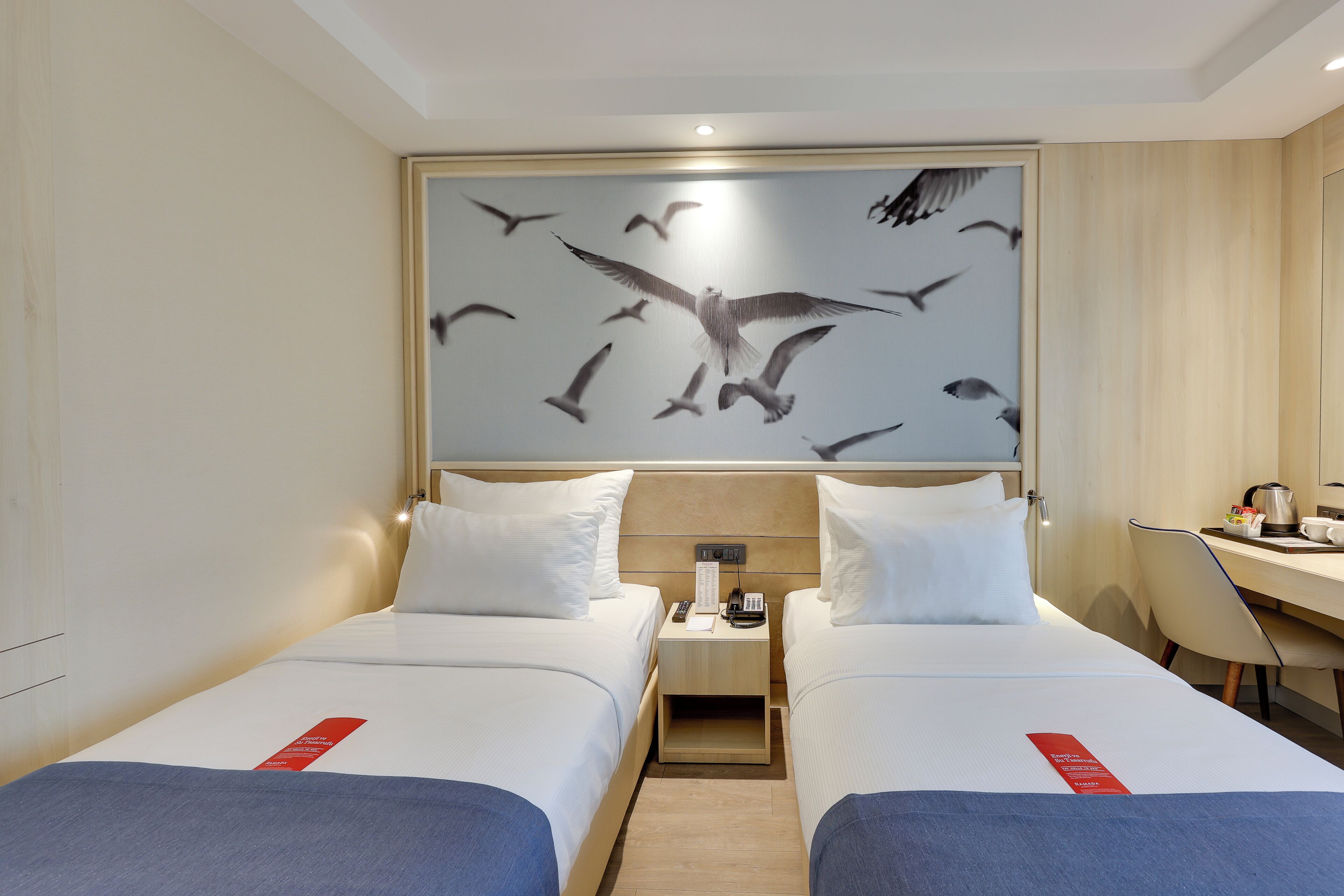 A hotel room with two beds, a desk, a chair, and a wall art of birds.