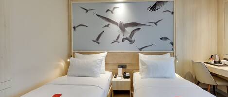 A hotel room with two beds, a desk, a chair, and a wall art of birds.