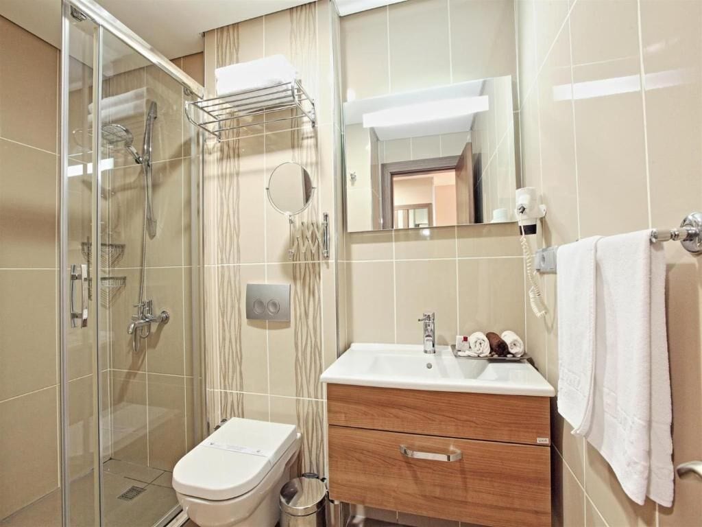 Un bagno moderno con doccia vetrata, un lavandino bianco con mobile contenitore in legno e uno specchio sopra il lavandino.