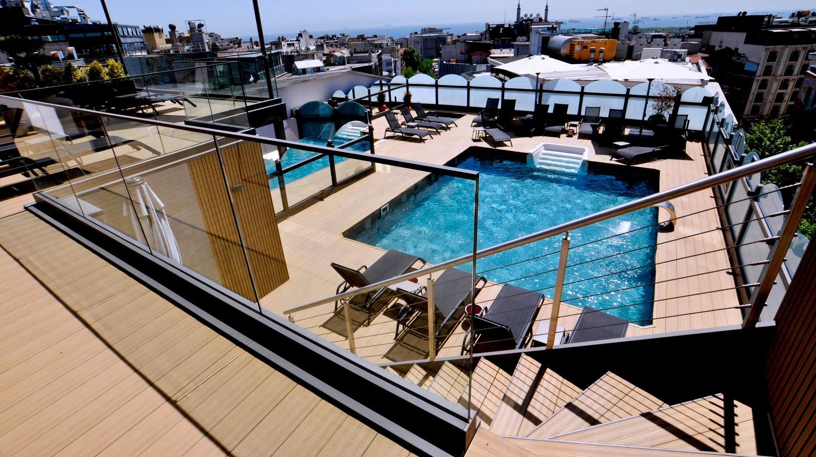 Un área de piscina en la azotea con sillones de descanso y barandilla de cristal.
