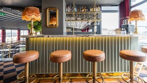 Zona de bar amb taulell de marbre, quatre tamborets, paret mirall i prestatgeria amb ampolles.