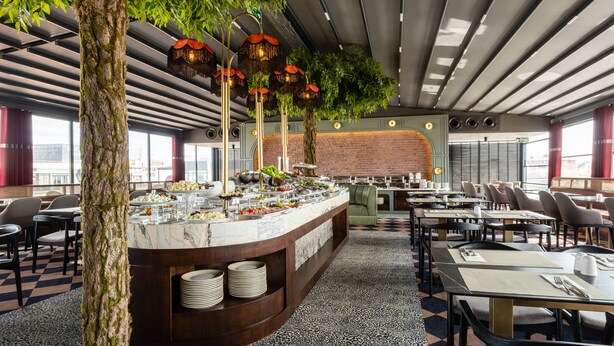 Un restaurant modern amb un taulell de marbre, plantes verdes i una paret de rajola. Taules i cadires disposades per dinar.
