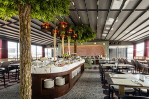 A modern restaurant with a marble counter, green plants, and a brick wall. Tables and chairs are arranged for dining. - Yigitalp Hotel (Istanbul)
