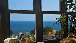 Une table à manger dressée avec des assiettes, des couverts et des verres, offrant une vue sur la mer grâce à de grandes fenêtres.