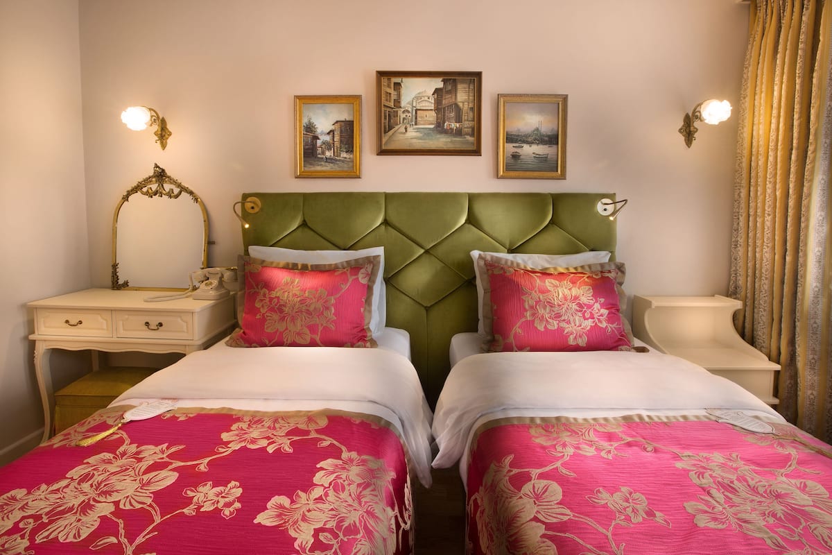 A double bed with floral bedding, a green upholstered headboard, and two bedside tables with lamps.