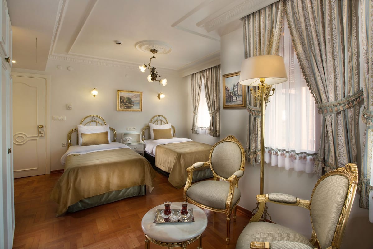 A hotel room with two beds, a sitting area with a table and chairs, and a large window with curtains.