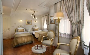 A hotel room with two beds, a sitting area with a table and chairs, and a large window with curtains.