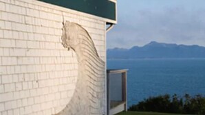 A building with a white brick exterior and a large, curved architectural feature resembling a wave. - The Ocean Shores (Homer)