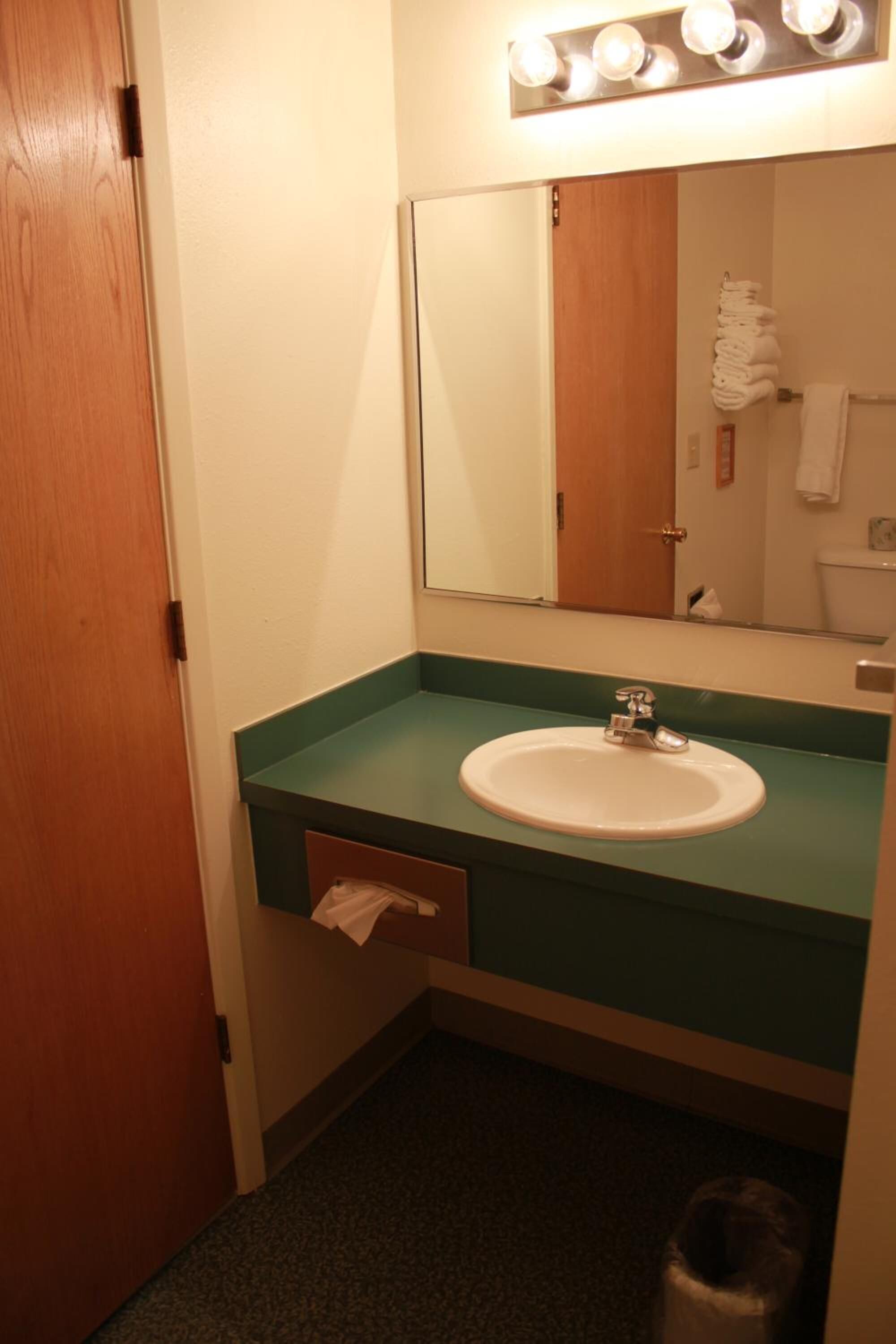 A bathroom with a green countertop, a white sink, a mirror, and a towel rack.