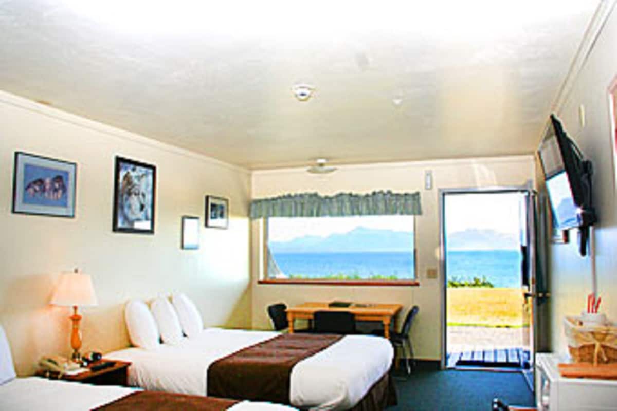A hotel room with a bed, bedside table, lamp, and a window with a view of the sea.