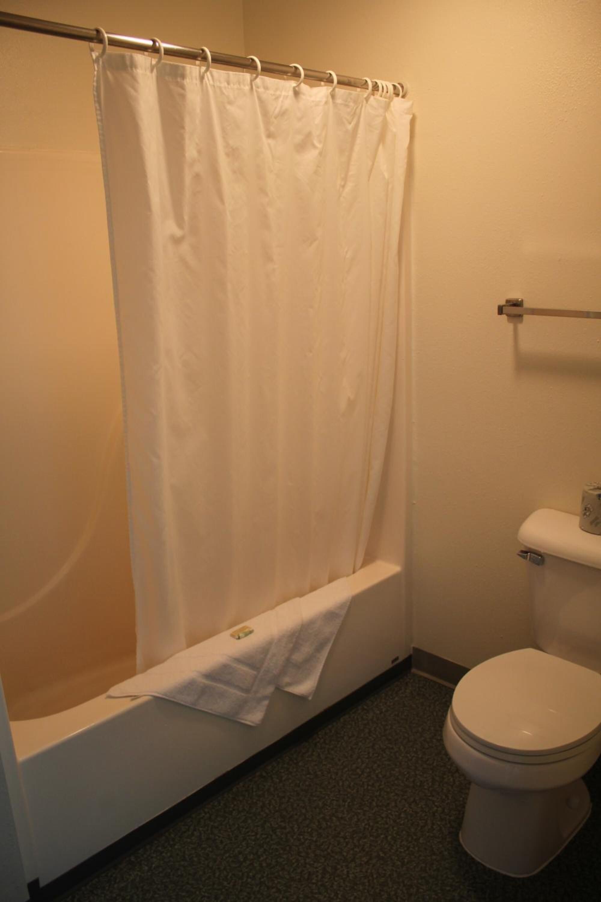 A bathroom with a shower curtain, a bathtub, a toilet, and a towel rack.
