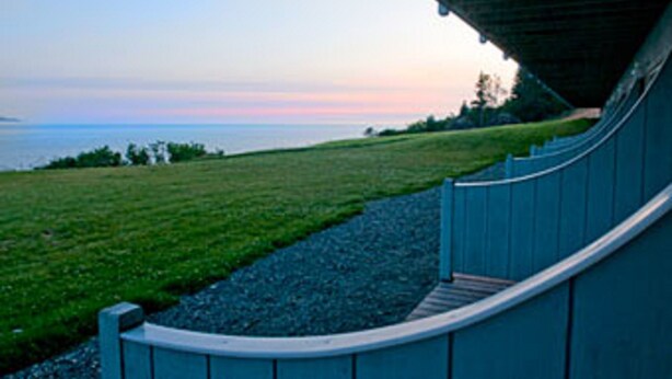 A curved pathway under a bridge with a view of the sea and a grassy area. - The Ocean Shores (Homer)