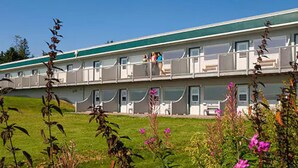 A motel with a green roof, multiple balconies, and a grassy lawn with flowers. - The Ocean Shores (Homer)