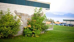 A building with a brick facade, a green roof, and a view of mountains in the background. - The Ocean Shores (Homer)