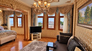 A luxurious room with a large bed, a sofa, a television, and a painting.