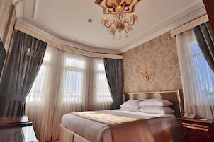 Una habitación de hotel con una cama grande, una araña y cortinas en las ventanas.