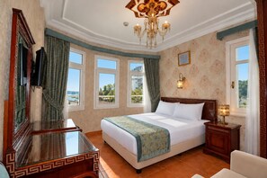 Habitación de hotel con una cama grande, un escritorio, una silla, un candelabro y vistas al exterior.