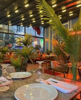 Ein Restaurantinnenraum mit gedeckten Tischen, Zimmerpflanzen und einem modernen Deckenstil.
