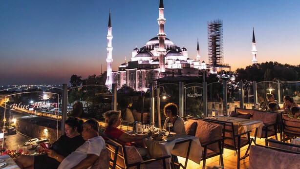 A rooftop restaurant with outdoor seating overlooking a historic building with multiple minarets. - Blue House Hotel (Istanbul)
