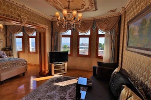 Ein luxuriöses Zimmer mit einem großen Bett, einer Couch, einem Fernseher und einem Gemälde an der Wand.