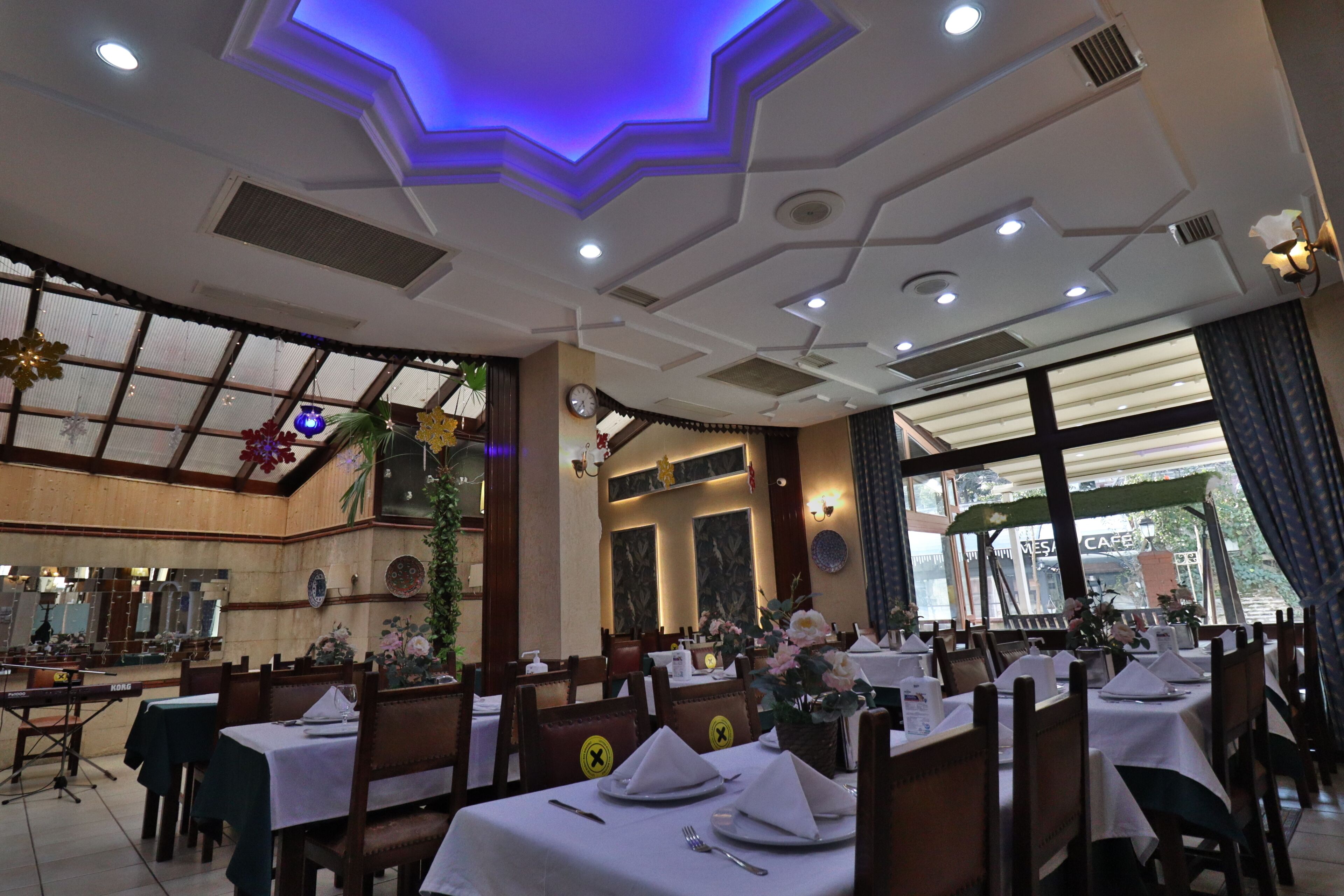 A restaurant with tables set for dining, a large window with a view, and a decorative ceiling.