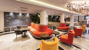 Un lobby moderno con zona de estar, sillones naranja y amarillos, una mesa redonda y un techo decorativo.