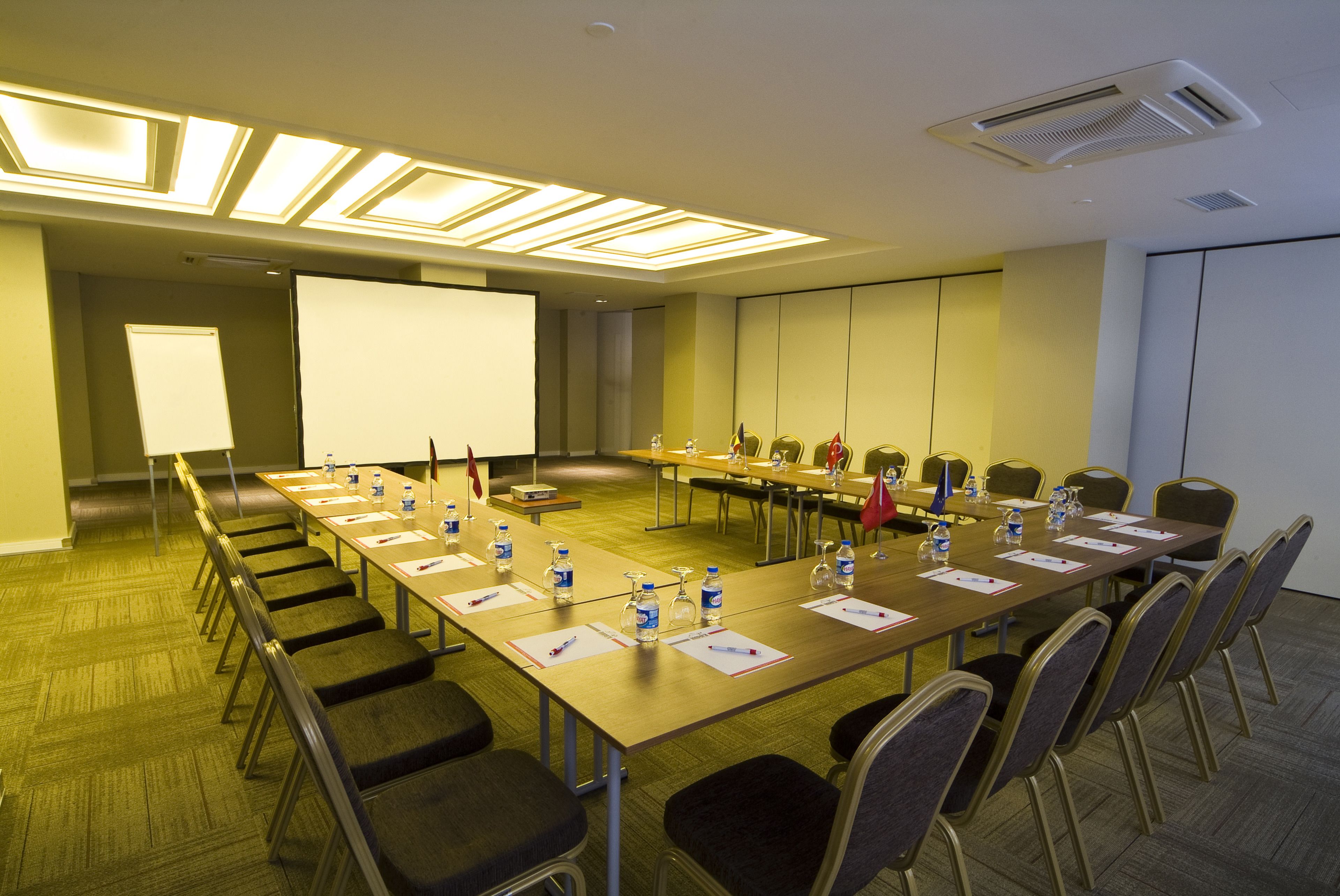 A conference room with a long table, chairs, water bottles, and a projector screen.