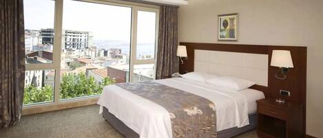A hotel room with a large bed, two bedside lamps, a nightstand, and a window with a city view.