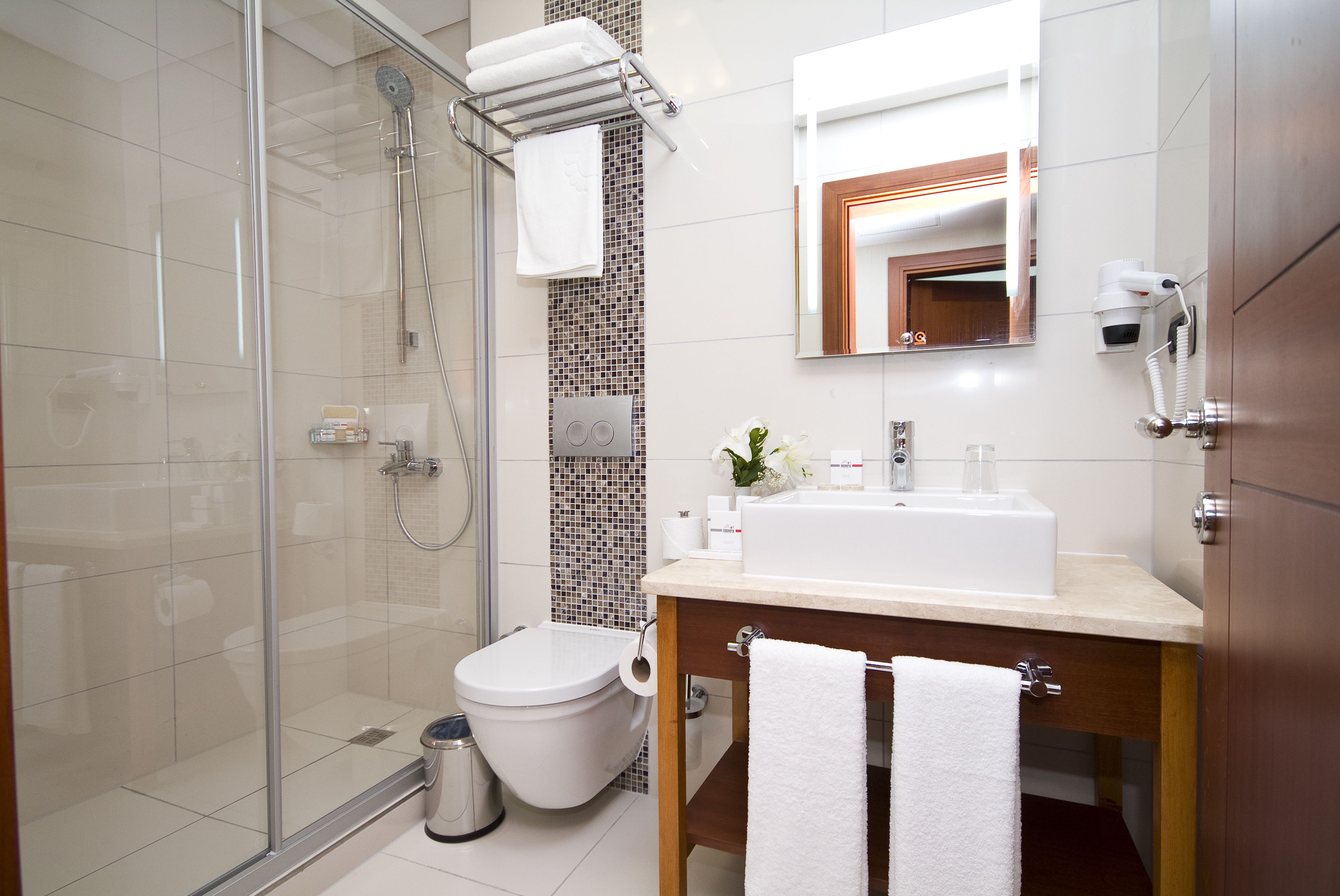 Une salle de bain moderne avec une douche à parois de verre, des toilettes, un lavabo avec un miroir au-dessus et un porte-serviettes.