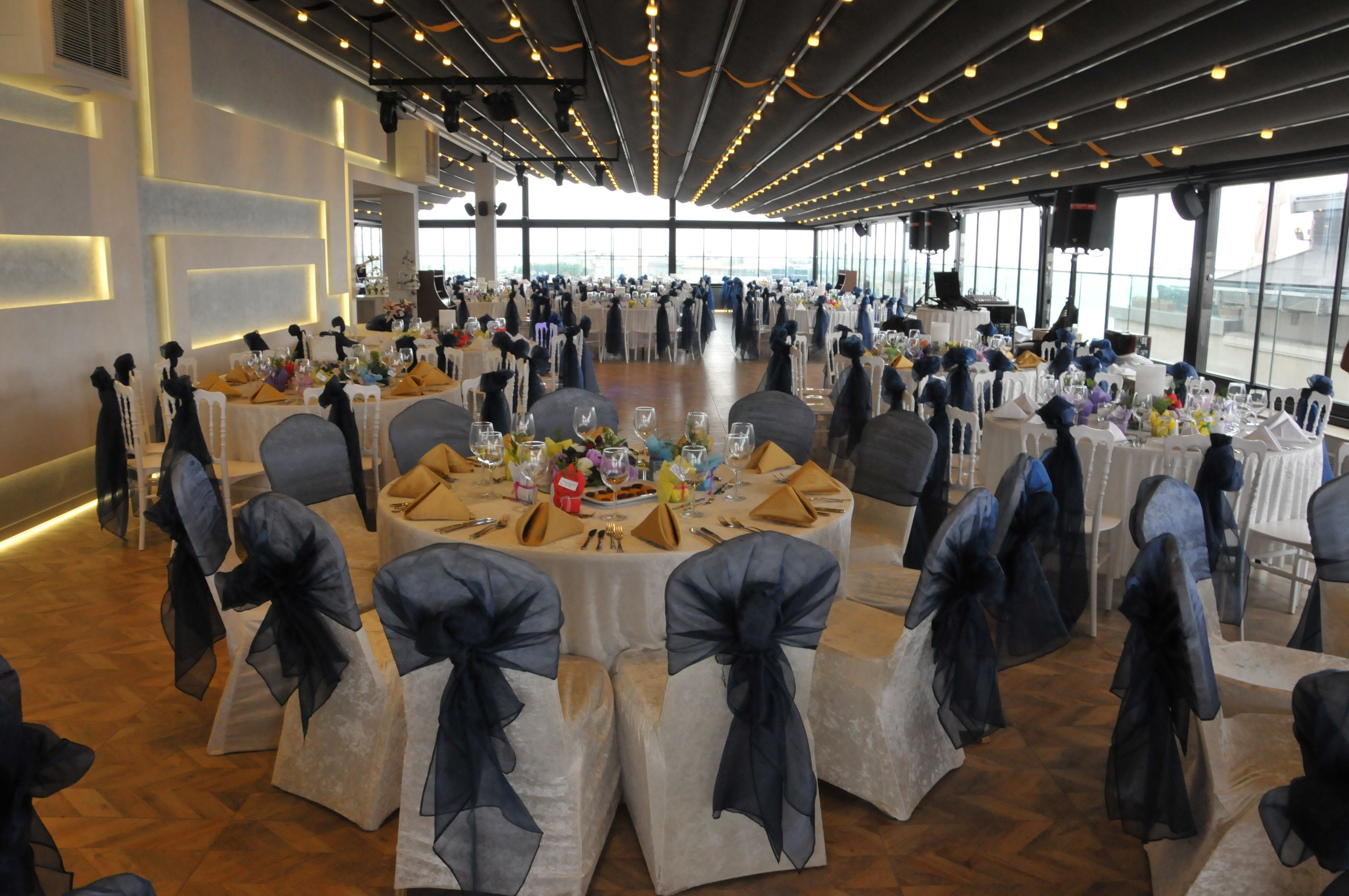 A spacious indoor venue with round tables, chairs with black sashes, and a modern ceiling design.