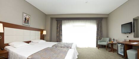 Une chambre d’hôtel avec un grand lit, deux tables de chevet, un bureau avec une chaise, une télévision et un mini-bar.